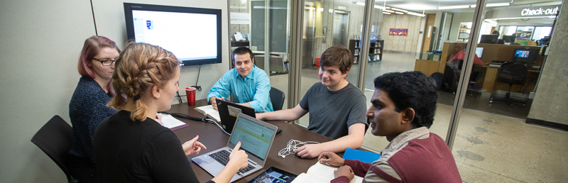 Five students working together inside a bookable study rooms on the ground floor of the Murray Library.